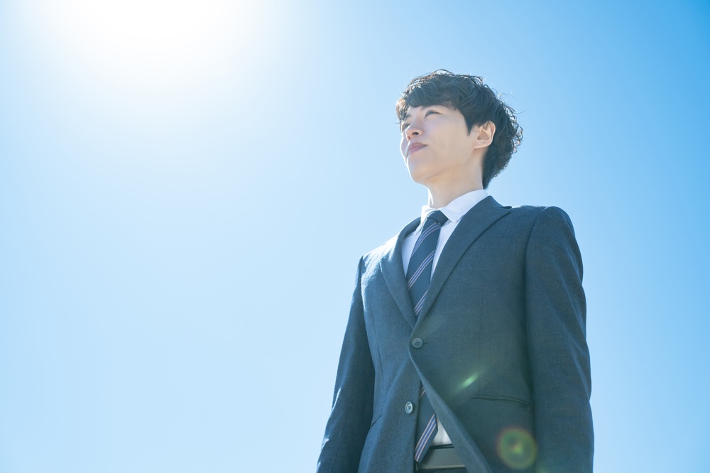 青空を見上げるスーツの男性